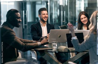 Smiling colleague looking at businesswoman while sitting in meeting at office