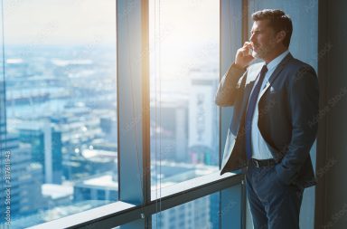 Mature business CEO talking on phone alongside large high windows